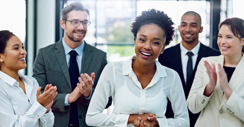 A diverse group of employees smiling and celebrating a coworker in an office setting.
