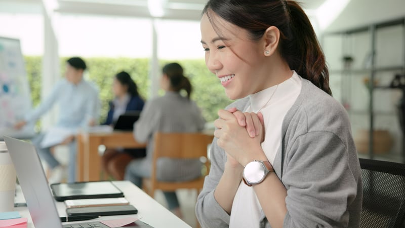 Happy female employee looking at computer reading about her company's employee incentive programs