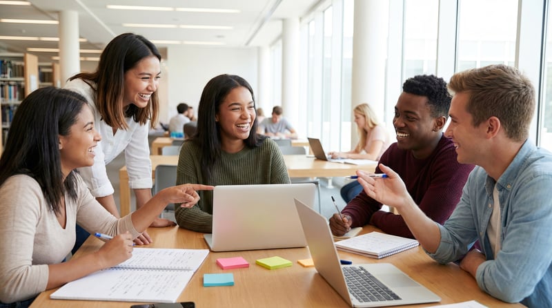 Coworkers collaborate around a workshop table with laptops, notebooks, and colorful sticky notes to map out an employee recognition program. 