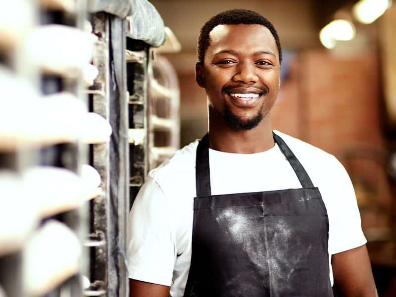 Bakery worker smiles proudly by the oven, representing frontline talent worth celebrating
