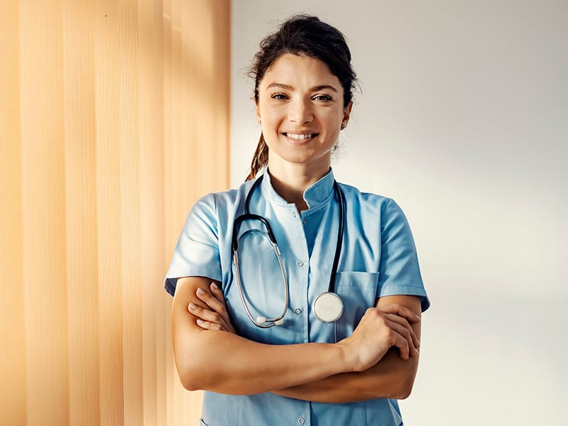 Confident nurse in scrubs stands smiling with arms crossed, ready to serve