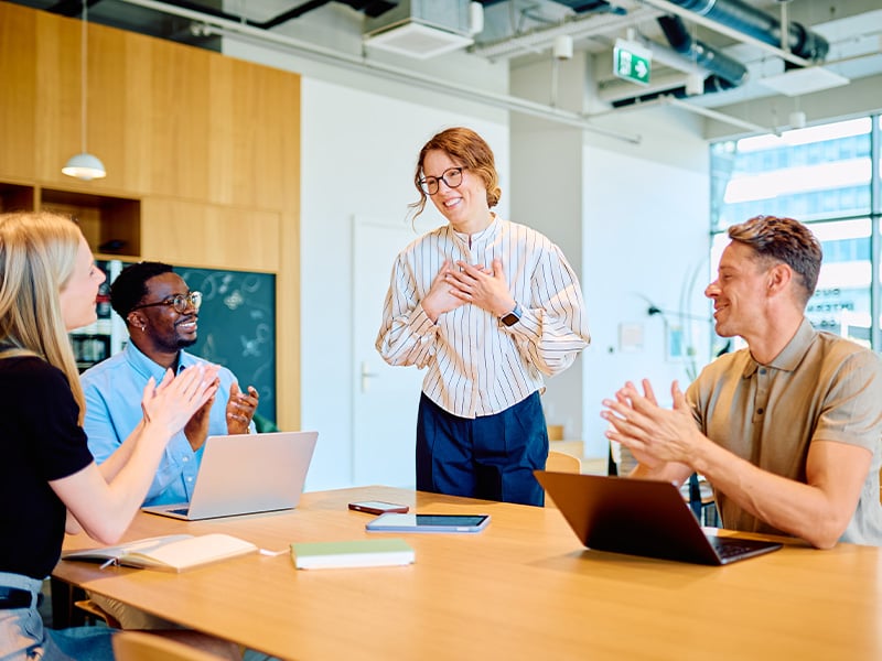 Employee touched and grateful as her team applauds her during an office meeting