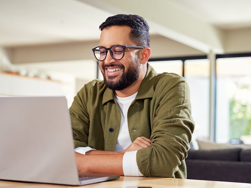 Engaged employee laughing while working on his laptop at home