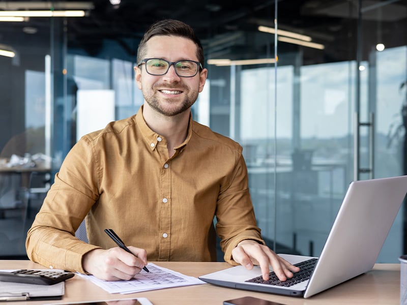 Engaged employee smiling at his desk with a laptop in a modern office