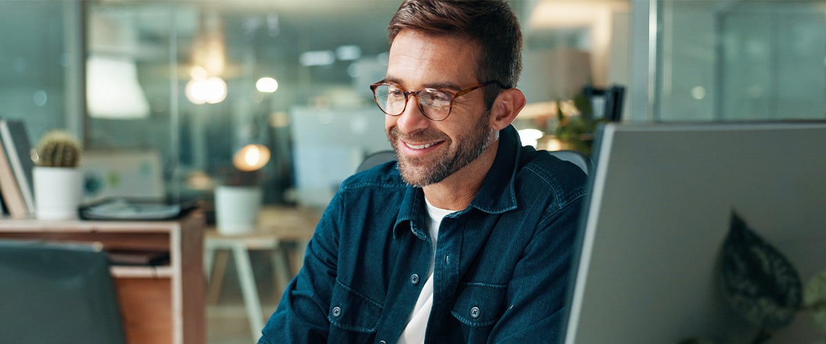 Engaged employee smiling while working at his computer in a cozy modern office