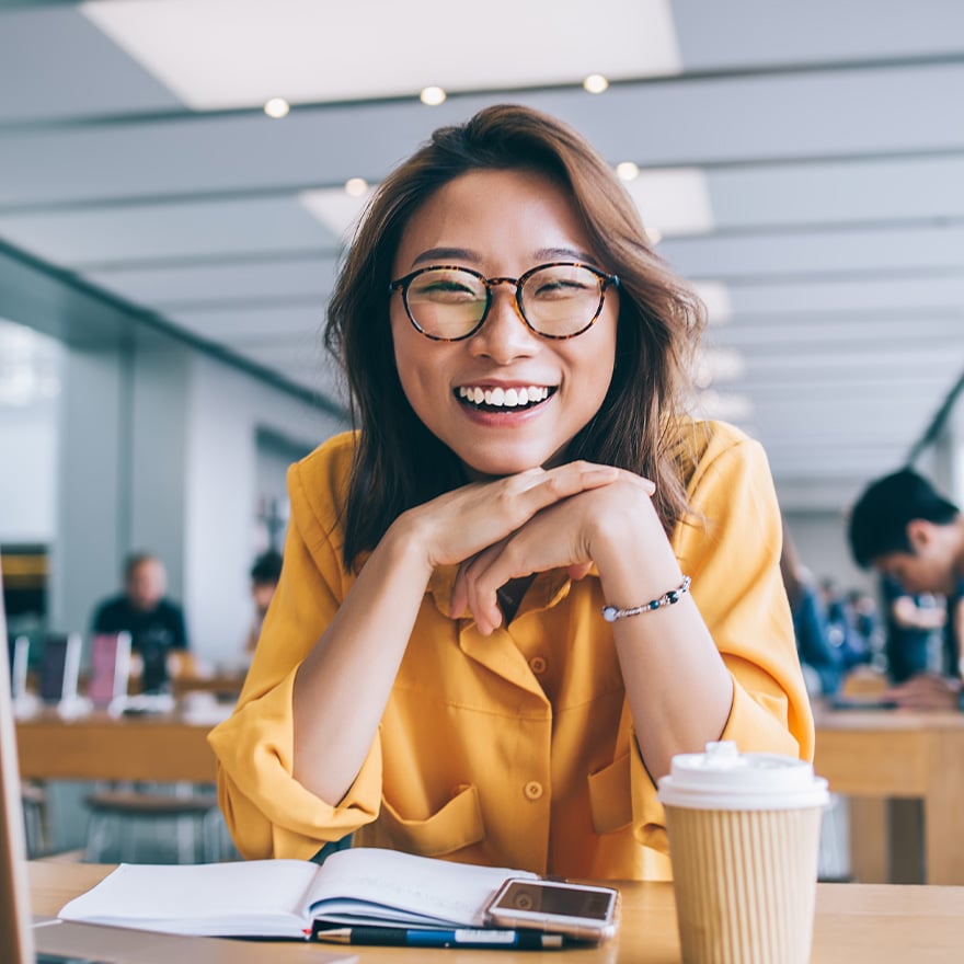 Enthusiastic employee smiling brightly at her laptop in a busy open workspace