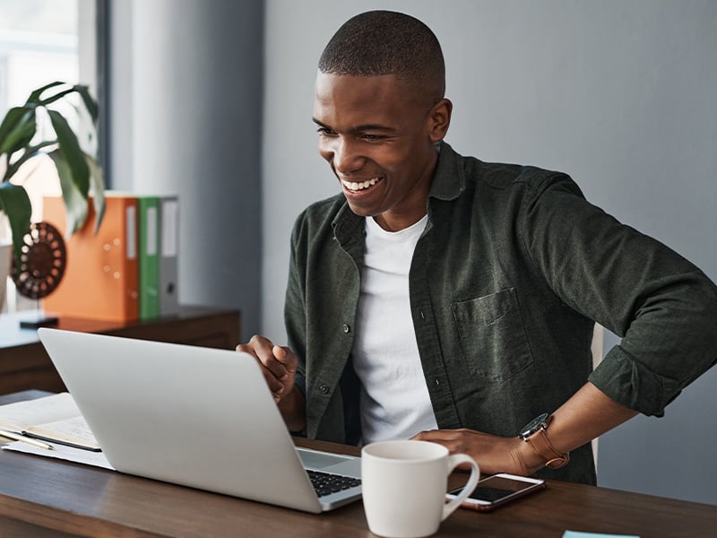 Excited employee reacting with joy to great news on his laptop at his desk