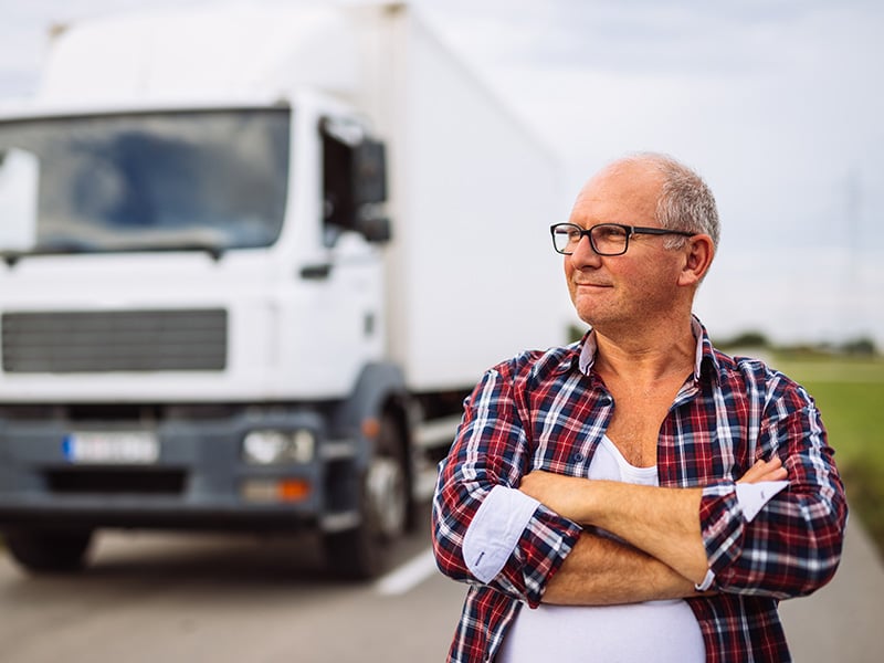 Experienced truck driver standing arms crossed confidently in front of his truck