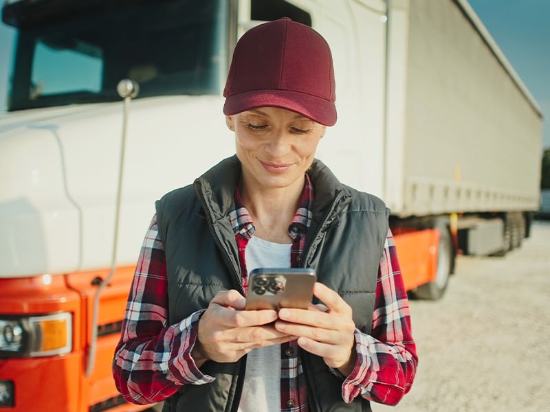 Female truck driver smiling while checking her phone in a transportation yard
