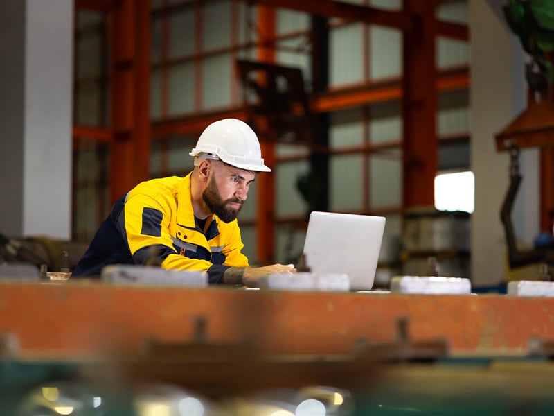 Focused technician in a hard hat reviews data on a laptop in a factory setting