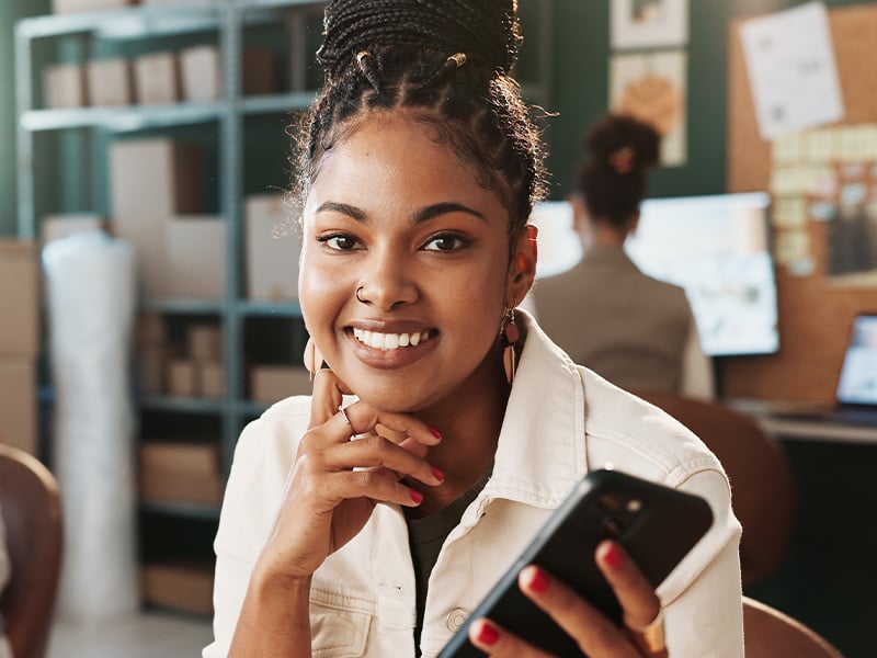 Happy employee smiling at the camera while holding her phone at work