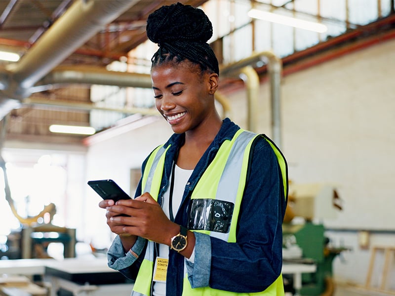 Happy engineer in factory for inventory, storage or text for furniture production, using her phone_