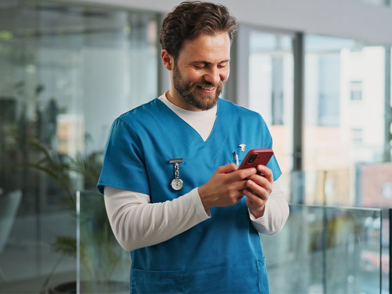Healthcare worker in scrubs smiling while checking recognition on his phone
