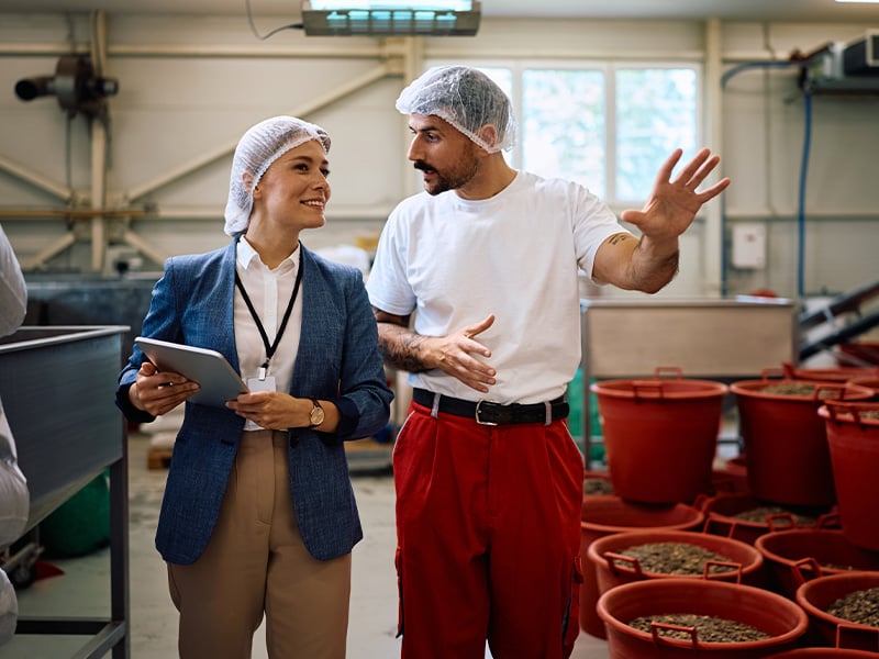 Manager and production employee discuss operations near bins, showing collaborative team culture