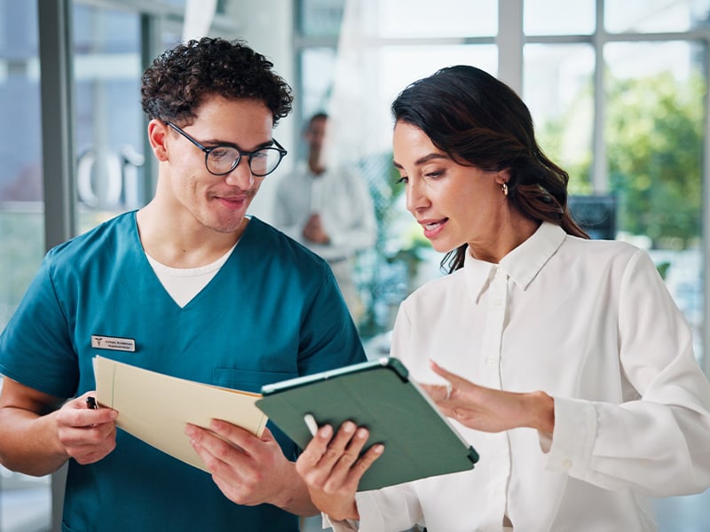 Nurse and colleague review notes on a tablet together, collaborating on patient care