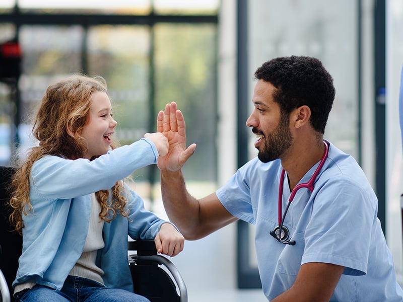 Nurse and young patient in a wheelchair share a joyful high five together