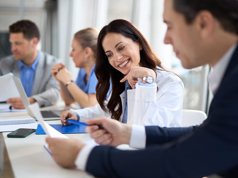 Physician smiles while reviewing a document with a colleague in a busy office setting