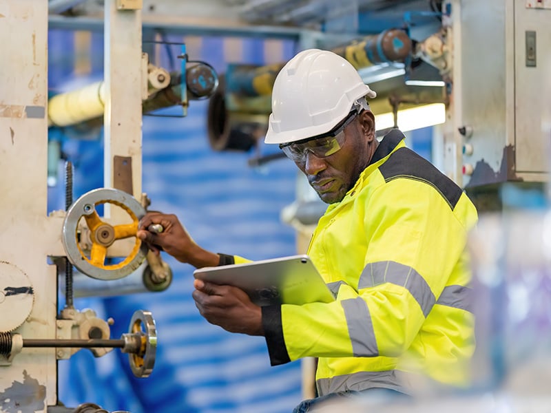 Safety-focused employee adjusts industrial equipment while reviewing data on a tablet