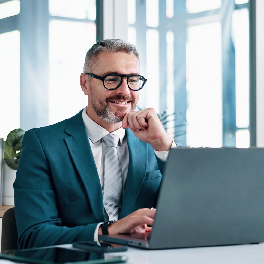 Satisfied business leader smiling while reviewing results on his laptop at his desk