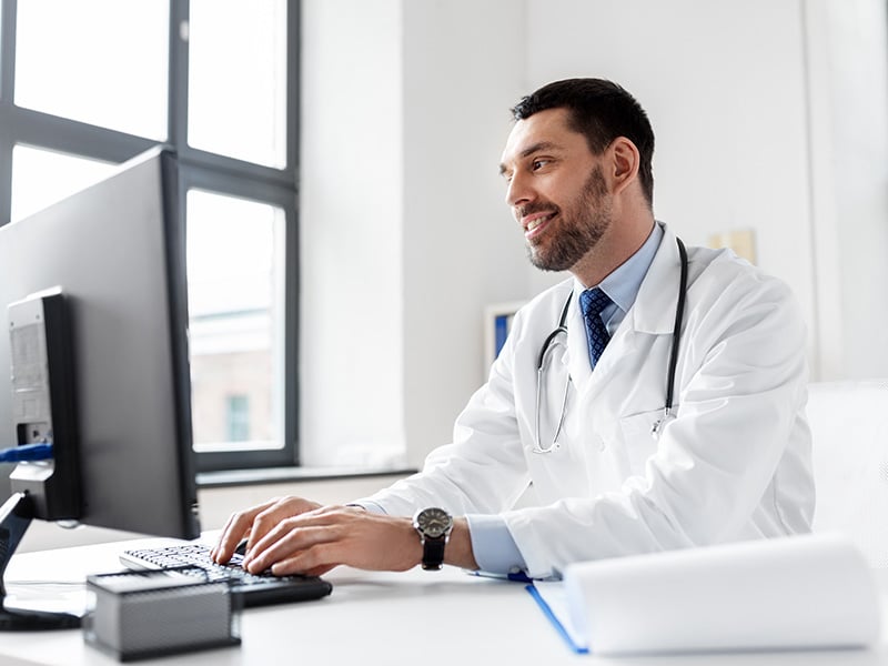 Smiling doctor in a white coat working at his computer in a bright office