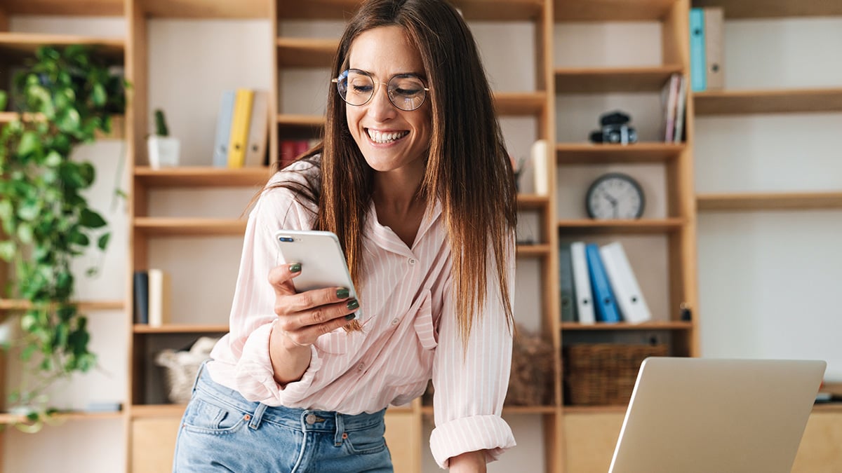Smiling employee checks her phone at her desk, staying connected and engaged