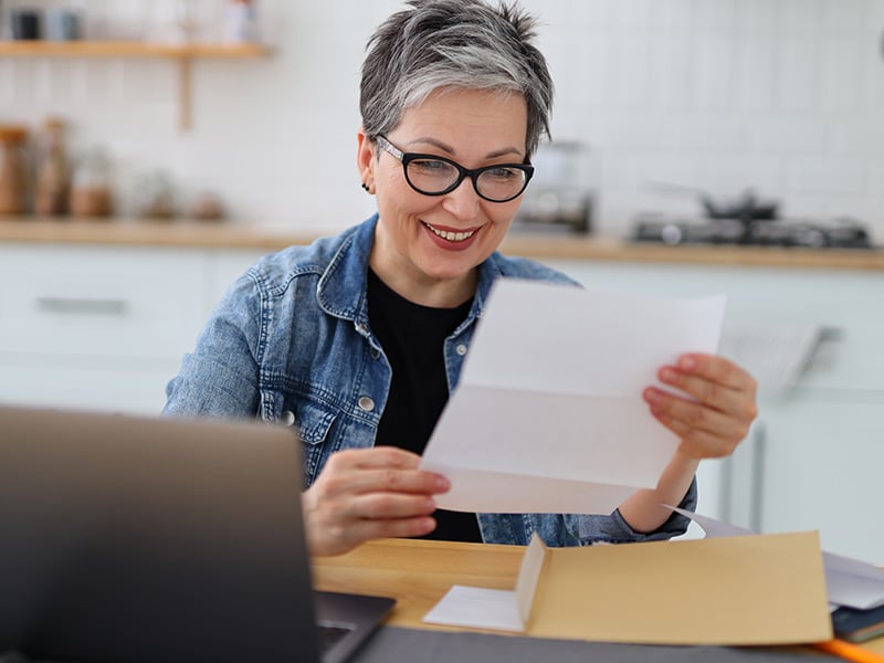 Smiling employee happily reviewing a document at her desk with a laptop nearby