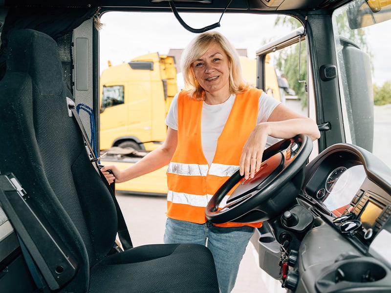 Smiling female truck driver in safety vest standing confidently inside her cab