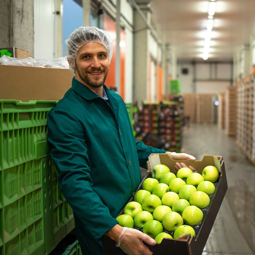 Smiling food production worker holding a box of fresh apples in a distribution warehouse