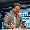 Smiling male businessman looking on phone while working on laptop in modern office space