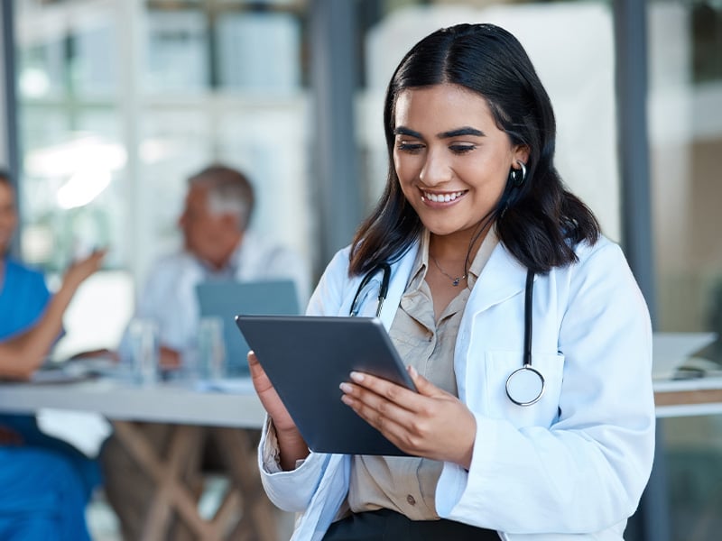 Smiling physician reviews patient information on a tablet, embodying attentive care