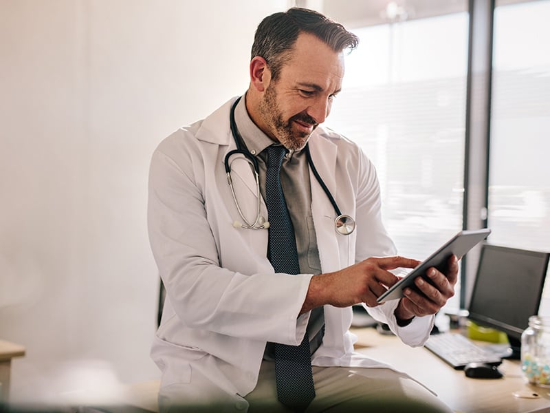 Smiling physician reviews patient records on a tablet in a sunlit office