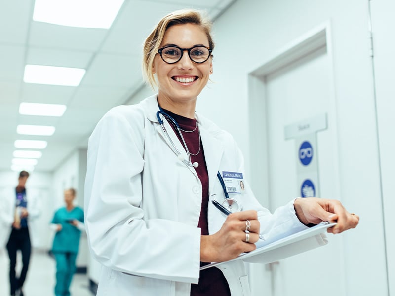 Smiling physician takes notes on a clipboard while walking through a hospital hallway