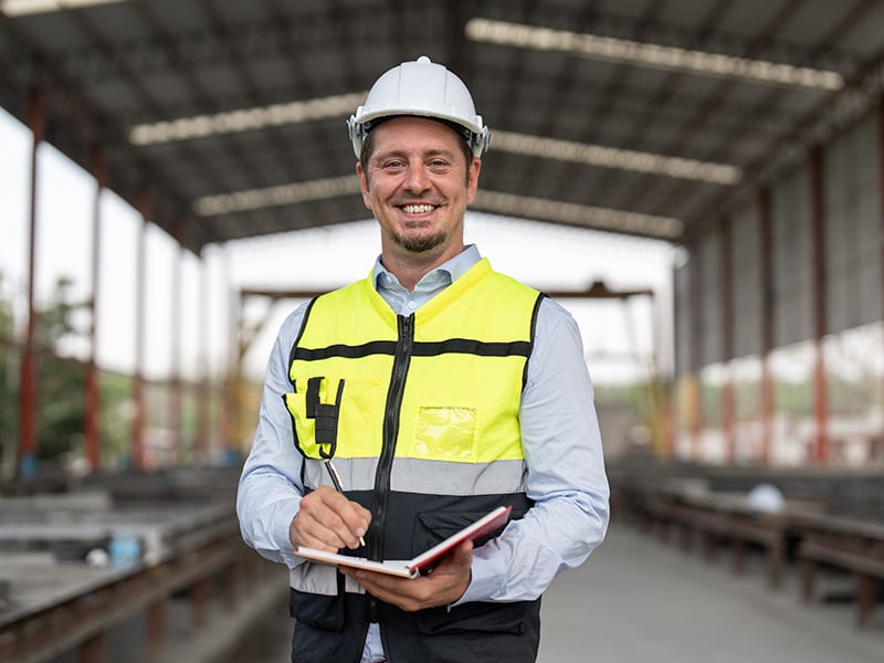 Smiling site manager takes notes on a clipboard inside an open construction warehouse