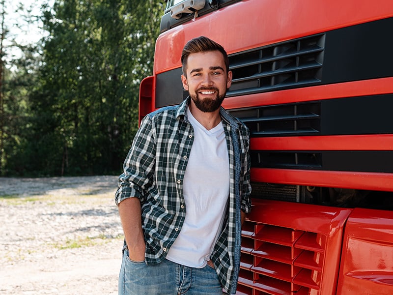 Smiling truck driver leaning casually against the front of his red truck