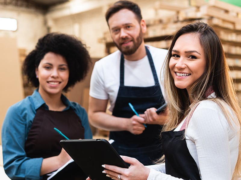 Smiling warehouse team collaborates with a tablet, reflecting engaged, connected workplace culture