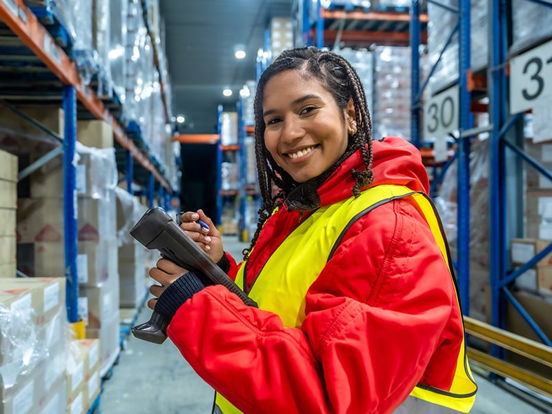 Smiling warehouse worker in safety vest holding a scanner on the floor