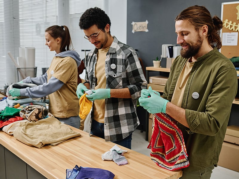 Three volunteers smiling while sorting donated clothing at a community drive
