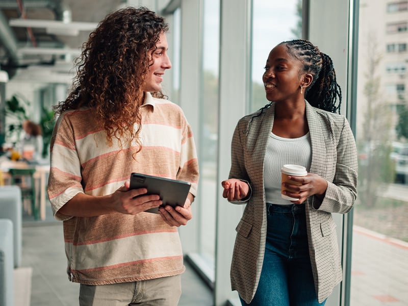 Two coworkers smiling and connecting over a tablet in a bright modern office