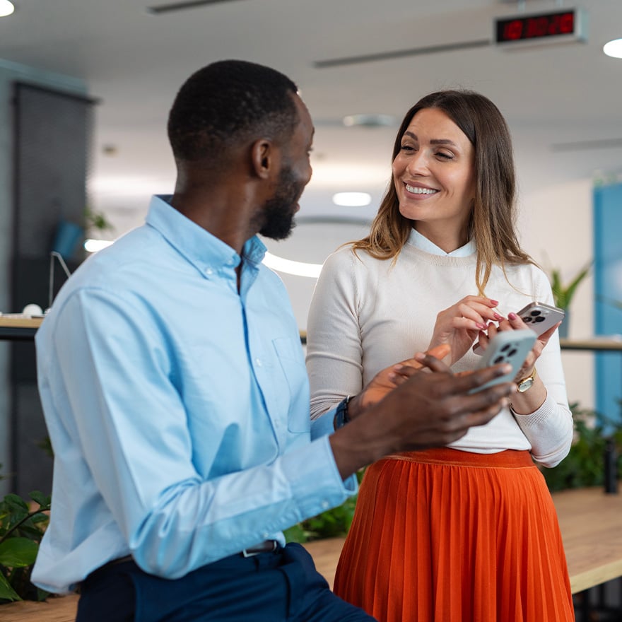 Two coworkers smiling and sharing a recognition moment on a phone at work