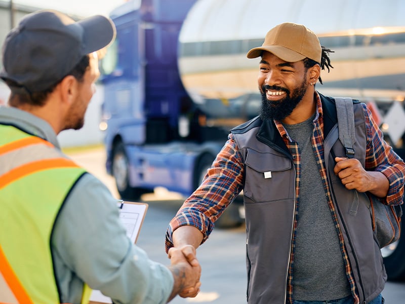 Two logistics workers sharing a warm handshake outside near a truck