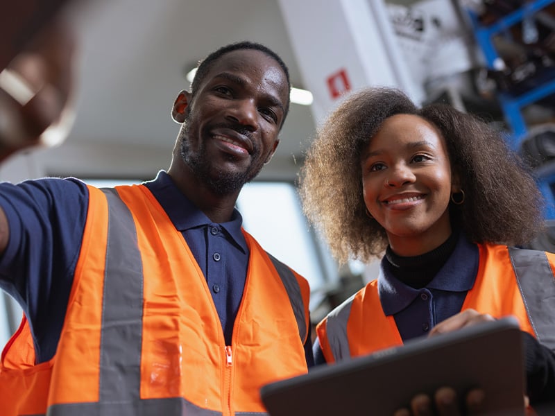 Two smiling coworkers in safety vests pose for a selfie, celebrating team spirit
