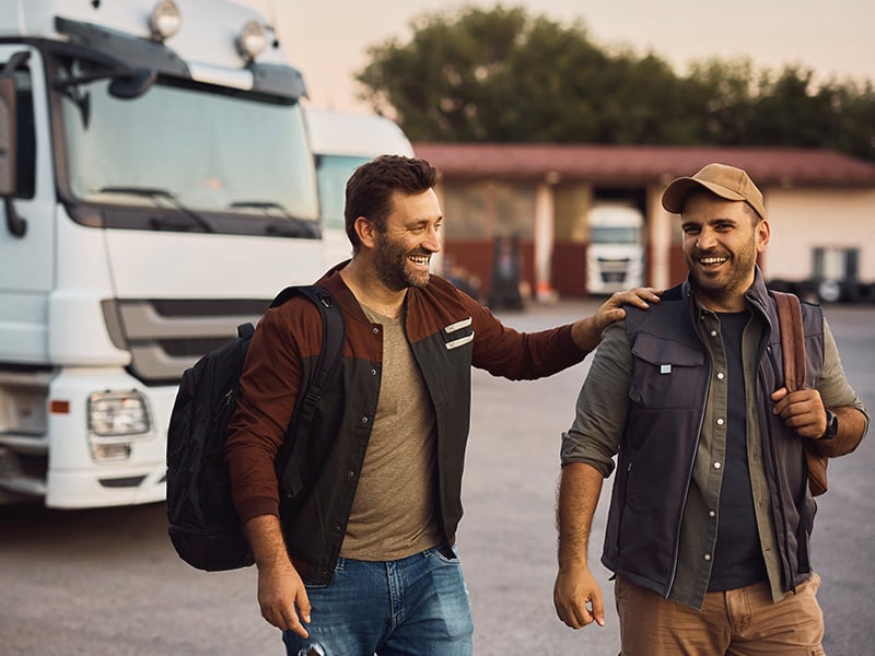Two truck drivers laughing and walking together in a transportation yard