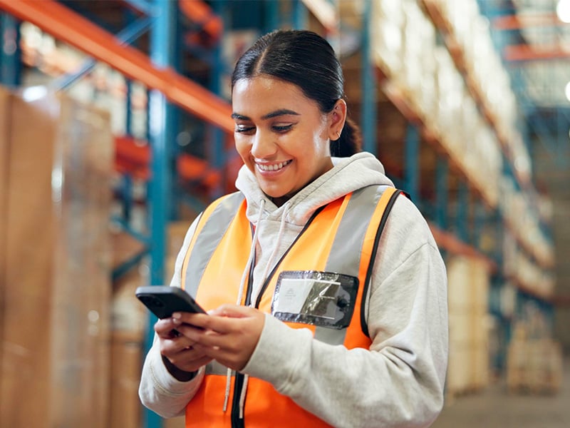 Warehouse worker in safety vest smiling while checking recognition on her phone