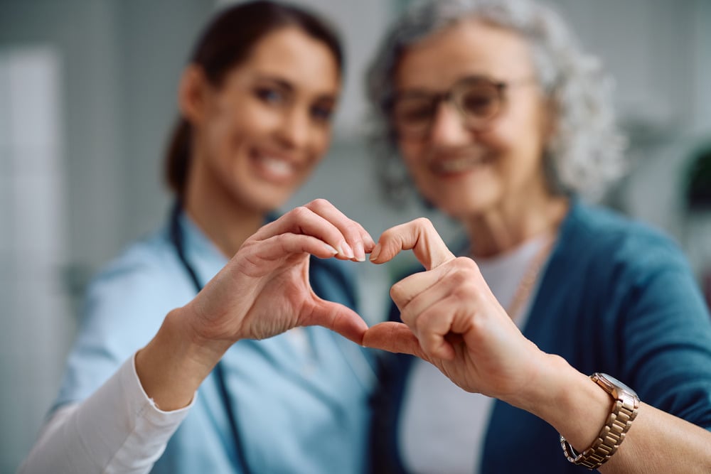 Healthcare worker and elderly patient making a heart shape with their hands together, symbolizing compassionate care and appreciation.