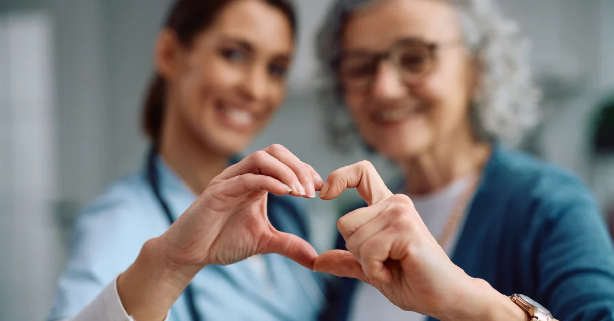 Healthcare worker and elderly patient making a heart shape with their hands together, symbolizing compassionate care and appreciation.